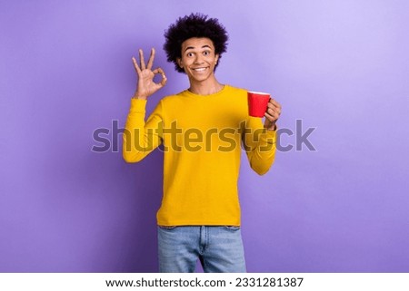 Portrait of satisfied good mood guy wear stylish yellow pullover showing okey hold cup of coffee isolated on violet color background