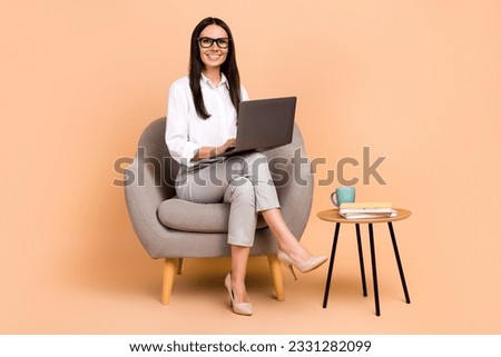 Full size photo of cheerful data analytic worker young lady sit chair with netbook remote communicating isolated on beige color background