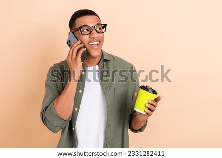 Photo of dreamy funky man wear khaki shirt spectacles drinking tea talking gadget empty space isolated beige color background