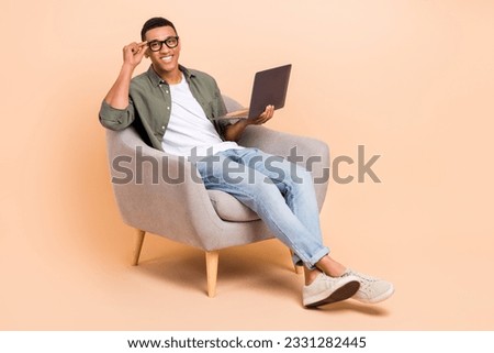 Full length photo of funky cool guy dressed khaki shirt siting chair texting modern device empty space isolated beige color background