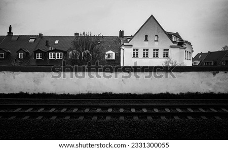 Monochromatic photo of house, wall, and railroad. Rural architectural landscape road travel photo in Berlin, Germany. 