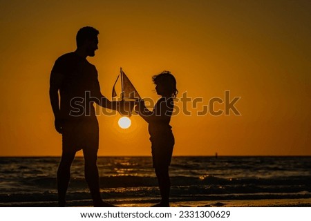 Son and father playing with toy boat in summer sea. Family dream on cruise liner. Travel, summer holiday. Journey trip. Dad and son playing with toy seailing boat on sunset sea. Fathers day.
