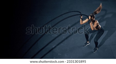 Effective Workout with a rope. Sportswoman trains in the functional training gym, performing crossfit exercises with a battle rope. Royalty-Free Stock Photo #2331301895