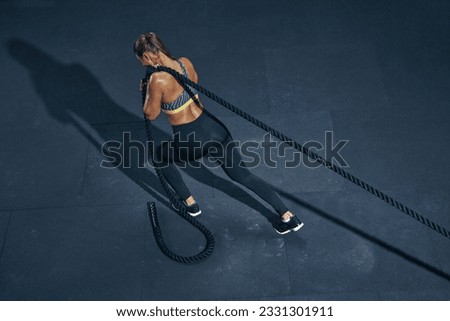 Female athlete fitness rope pull training. Sporty sportswoman working out in functional training gym doing cross exercise with battle rope. Royalty-Free Stock Photo #2331301911