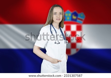 A young female doctor in a white coat and a stethoscope stands on the background of the flag of Croatia.