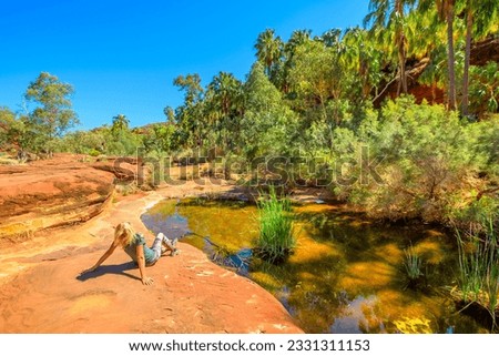 Tourist woman relaxing after trekking along Arankaia Walk in the heart of Palm Valley Oasis waterhole, Finke Gorge National Park. Tourism in Australian Outback, Northern Territory, Central Australia Royalty-Free Stock Photo #2331311153