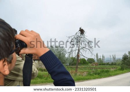 The boy is bird-watching. The boy observes the storks in the nest with binoculars. Royalty-Free Stock Photo #2331320501