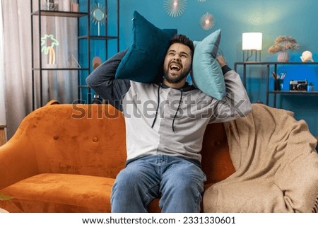 Repair work at neighbours. Irritated young man relaxing on couch cover ears with pillows annoyed by noisy neighbors suffer from headache wish silence. Thin walls at home flat without sound insulation Royalty-Free Stock Photo #2331330601