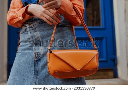 Street fashion details: woman wearing trendy summer outfit, carrying orange color faux patent leather baguette bag. Copy, empty space for text  Royalty-Free Stock Photo #2331330979