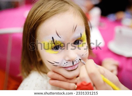 Face painting for cute little gorl during kids merriment. Face paint for "Animals" theme on birthday party. Preschooler kids celebrating party in entertainment center. Child in amusement park