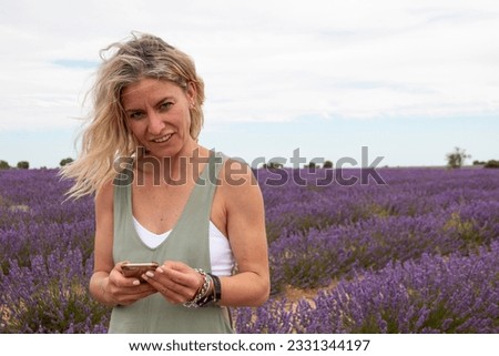 Blonde woman with mobile phone in hand enjoying her summer vacation in a blooming field of lavenders