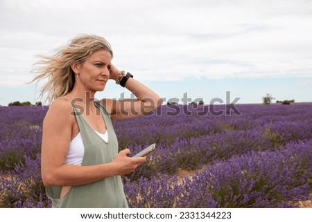 Blonde woman with mobile phone in hand enjoying her summer vacation in a blooming field of lavenders