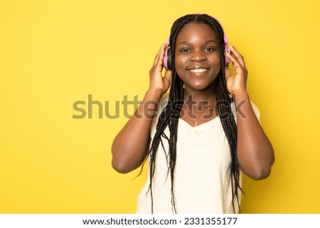 young African American woman listening music in headphones and dancing in front of yellow background