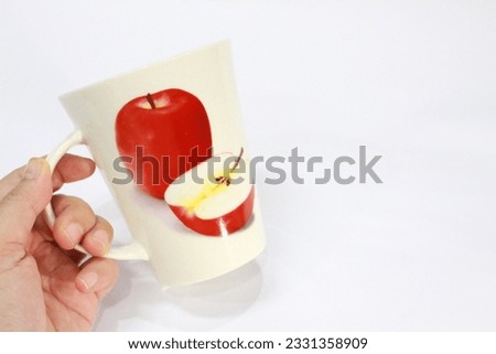 Hand holding a white glass with an apple picture on a white background