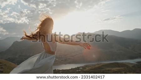 Woman in white dress standing on top of a mountain with raised hands while wind is blowing her dress and red hair - freedom, nature concept.Copy space