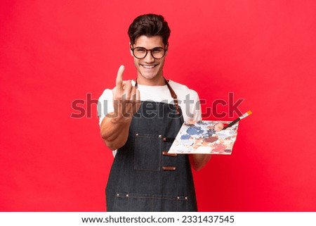 Young artist caucasian man holding a palette isolated on red background doing coming gesture