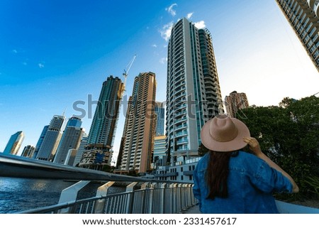 back view of a long hair woman in a hat watching the sunset over brisbane city; city reach boardwalk with amazing view of large skyscrapers by brisbane river, australia	

