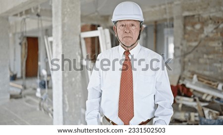 Senior grey-haired man architect standing with relaxed expression at construction site