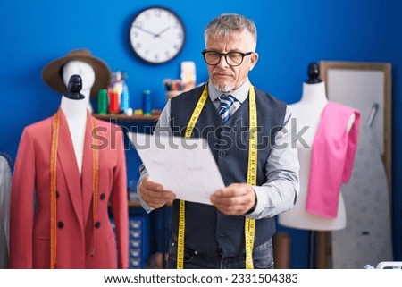 Middle age grey-haired man tailor reading document at clothing factory Royalty-Free Stock Photo #2331504383