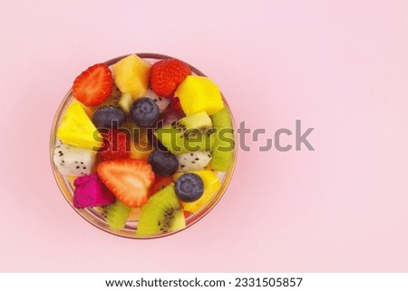 Fresh sliced fruits in bowl on pink background with space for text.