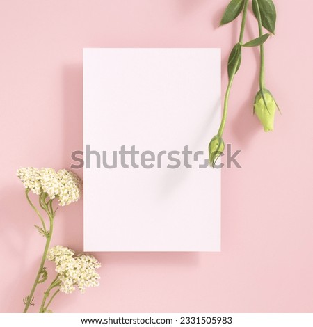 Greeting card mockup and white flowers on pink background top view flatlay. Card mock-up with copy space.