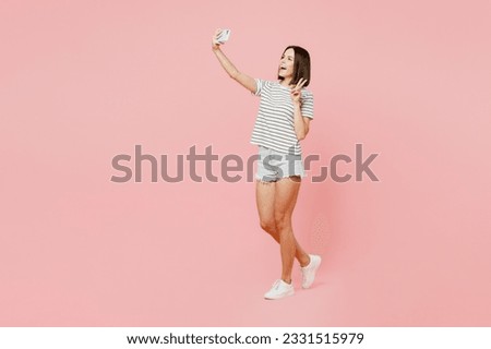 Full body young caucasian woman she wears casual clothes t-shirt doing selfie shot on mobile cell phone post photo on social network isolated on plain pastel light pink background. Lifestyle concept