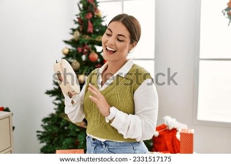 Young beautiful hispanic woman playing tambourine standing by christmas tree at home Royalty-Free Stock Photo #2331517175