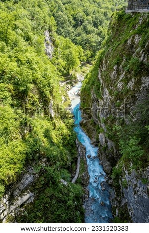 Top down view of Soca river canyon with steep, vertical cliffs covered in vegetation, deep in slovenian Alps and wooden bridge crossing the river
