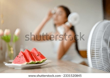 Close-up image of a plate with slide watermelons on a table with an overheated woman in the background. hot summer, heat attack, high temperature, live without air condition Royalty-Free Stock Photo #2331520845