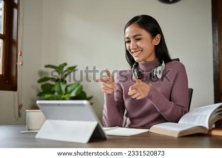 A cheerful Asian woman pointing her finger at the tablet screen, showing the correct or that's right hand sign while meeting online with her colleagues.