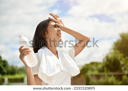 An exhausted and sweaty young Asian woman in sportswear is fighting the heat wave while running in a park on a sunny summer day. summer activity, heat stroke, dehydrated Royalty-Free Stock Photo #2331520895