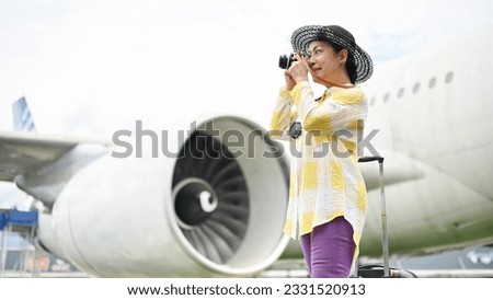 A happy and attractive senior Asian female tourist taking pictures with her film camera at the airport. summer vacation, tourist, trip, holiday, airplane