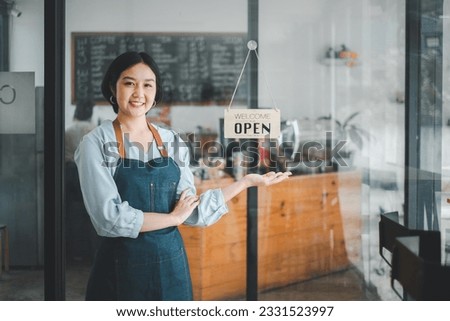 Portrait of happy waitress standing at restaurant entrance with open sign, Portrait of young business woman attend new customers in her coffee shop.
