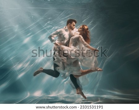 Real People art photo. Happy couple in love swim underwater, woman muse inspires male writer poet creator. Nymph girl dancing with guy at bottom sea under water. Red hair white long silk dress float. Royalty-Free Stock Photo #2331531191