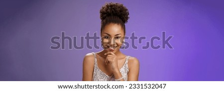 Intrigued creative young african-american devious 20s girl afro hairstyle in silver luxurious dress partying touching chin smirking mysterious have excellent idea inspired planning, blue background.