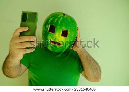shocked man looking at screen of mobile cell phone, wearing watermelon as helmet, hard hat on head and stylish sunglasses. male isolated on white wallpaper background. bad, breaking news. 
