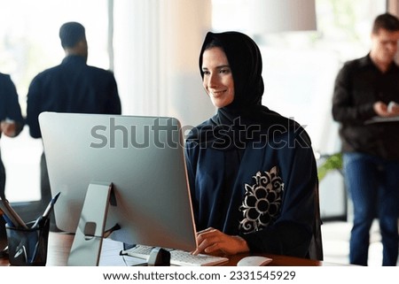 Selective focus on Emirati National woman in Abaya and Hijab at office using desktop computer display screen with blurred workmates as background. Emiratisation concept in the United Arab Emirates Royalty-Free Stock Photo #2331545929
