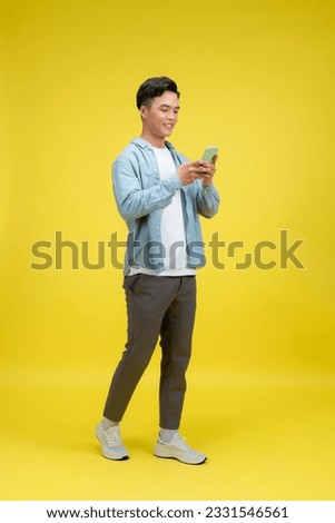 Happy man in casual wear using mobile phone chatting online, walking on yellow background Royalty-Free Stock Photo #2331546561