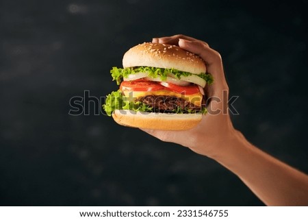 Tasty burger sandwich in hand isolated on black background 