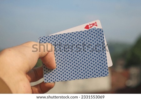 Photo of two cards held in one hand, one of which is upside down, only a king of hearts can be seen from a small gap