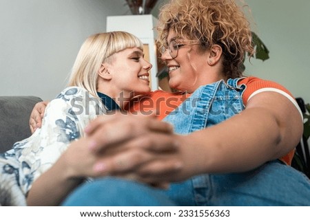 Portrait of a smiling lesbian couple sitting on sofa at home, embracing each other.