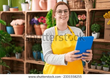 Young beautiful plus size woman florist smiling confident using touchpad at flower shop