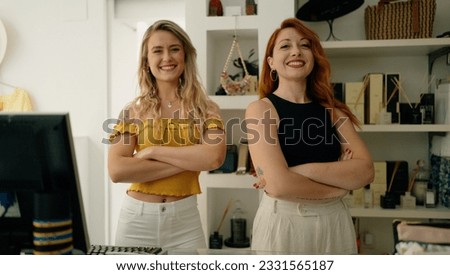 Two women shop employees standing with arms crossed gesture at clothing store