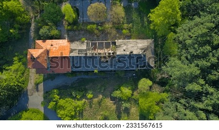 Destroyed abandoned large building in the forest in the mountains. Trees began to grow in the building, nature absorbs the structure. Top view from a drone, in early spring the whole forest is green