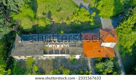 Destroyed abandoned large building in the forest in the mountains. Trees began to grow in the building, nature absorbs the structure. Top view from a drone, in early spring the whole forest is green