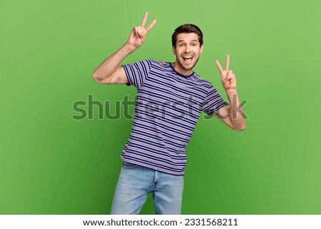 Portrait of optimistic positive pleasant guy with bristle wear striped t-shirt two hands showing v-sign isolated on green color background