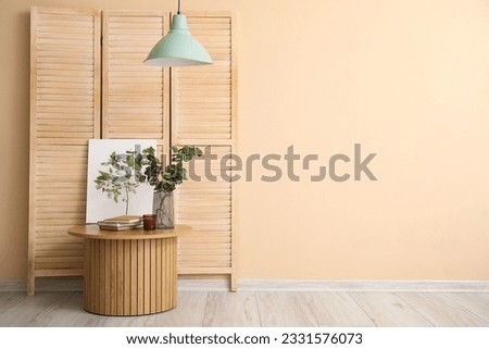 Coffee table with books, eucalyptus branches, picture of plant and folding screen near beige wall
