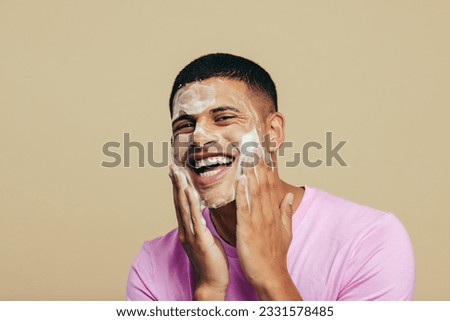 Portrait of a handsome young man indulging in his grooming and self-care routine as he applies face wash in a studio. Youthful man smiling happily while massaging his skin with a facial cleanser. Royalty-Free Stock Photo #2331578485