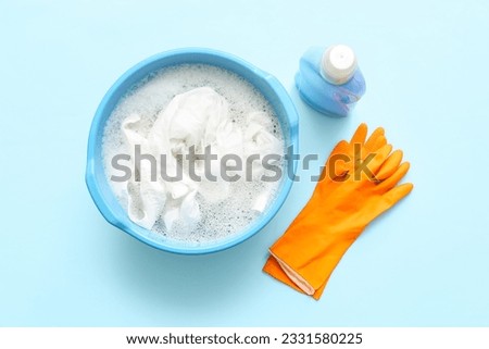 Plastic basin with dirty clothes, water, foam and orange rubber gloves on blue background Royalty-Free Stock Photo #2331580225