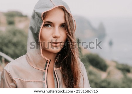 Woman rain umbrella. Happy woman portrait wearing a raincoat with transparent umbrella outdoors on rainy day in park near sea. Girl on the nature on rainy overcast day.